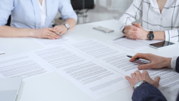 Business professionals reviewing important contract documents on a white desk, discussing legal details and negotiating terms during a corporate partnership meeting in an office setting